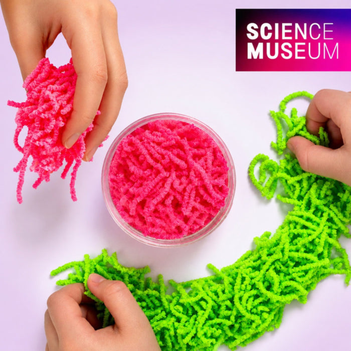 Hands play with neon green and bright pink squiggly toy worms next to a clear tub of pink worms on a purple background.