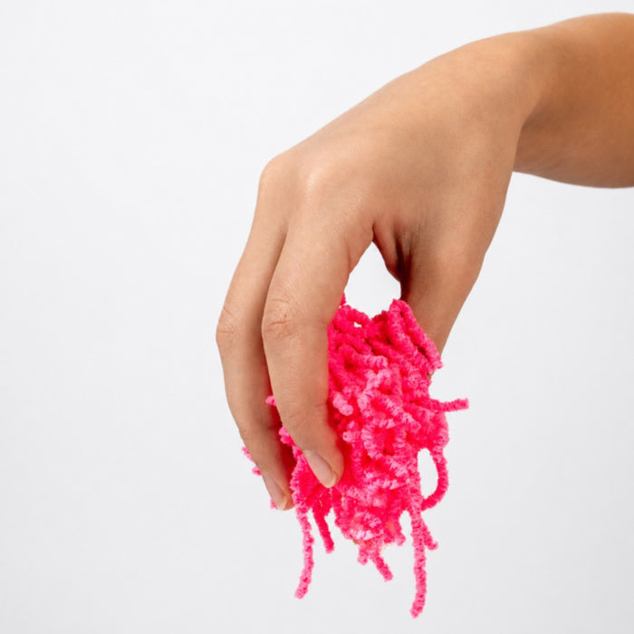 Hand holding a cluster of neon pink fuzzy worms with a shaggy, flexible texture against a white background.