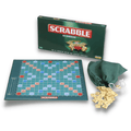 Green Scrabble As Gaeilge box, matching game board, and wooden tiles spilling from a green fabric drawstring bag.