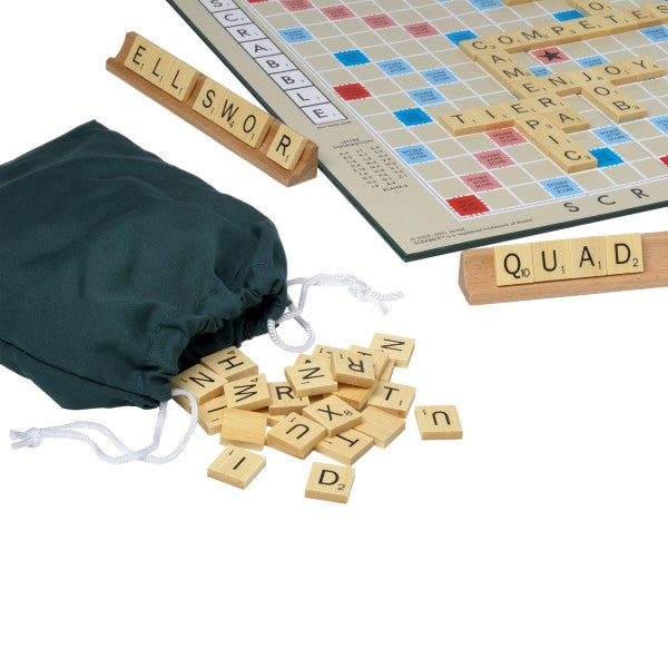 Scrabble board game with wooden letter tiles spilling from a green bag next to two wooden tile racks.