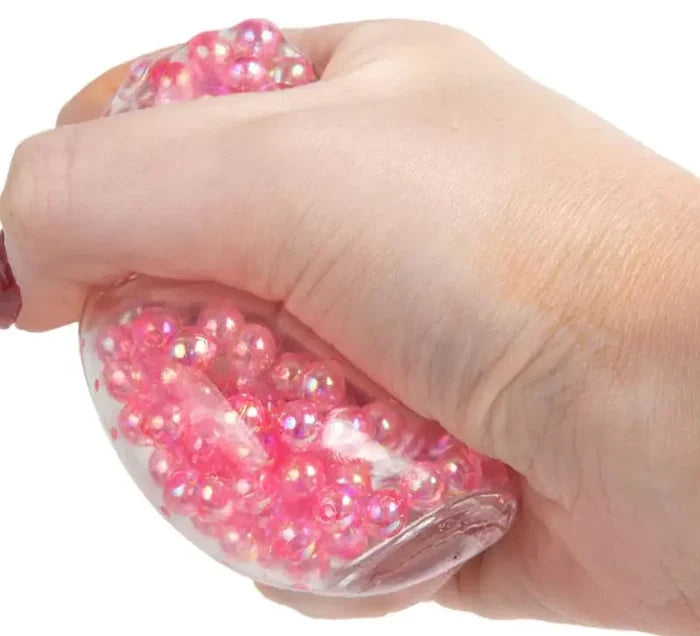 Hand squeezing a clear, soft cube filled with small, iridescent pink beads.