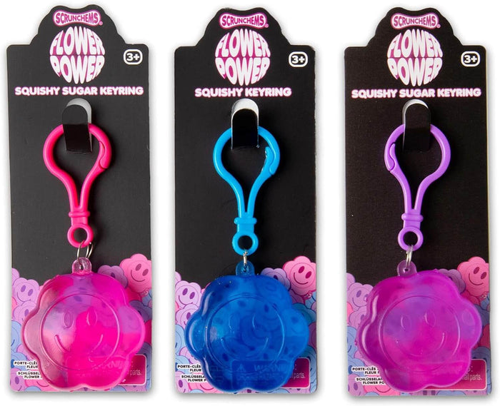 Pink, blue, and purple flower-shaped squishy keyrings with smiley faces on retail cards with matching plastic clips.