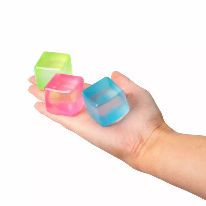Three translucent, squishy toy cubes in green, pink, and blue held in an open palm.