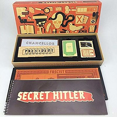 Open orange board game box revealing wooden President and Chancellor placards, game cards, and a spiral-bound rulebook.