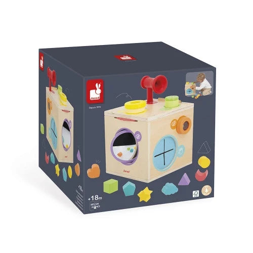 Dark blue box showing a wooden Janod sensory cube with a red horn, mirrors, and colorful shape icons for ages 18m+.