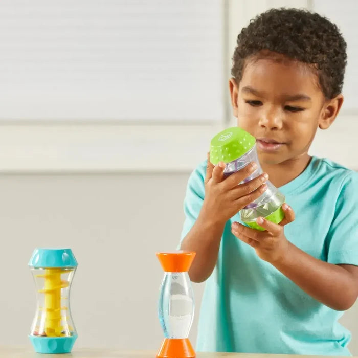 Child playing with three hourglass-shaped sensory tubes featuring colorful internal spirals, liquids, and beads.
