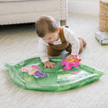 Baby pressing hands on a green leaf-shaped inflatable mat with water and floating colorful animal shapes inside.