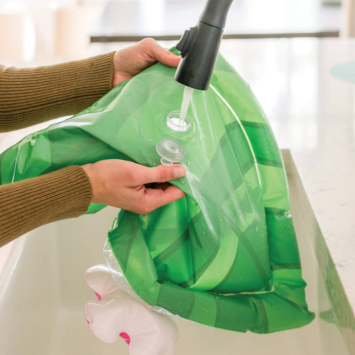 Hands filling a green patterned inflatable mat with water from a kitchen faucet.