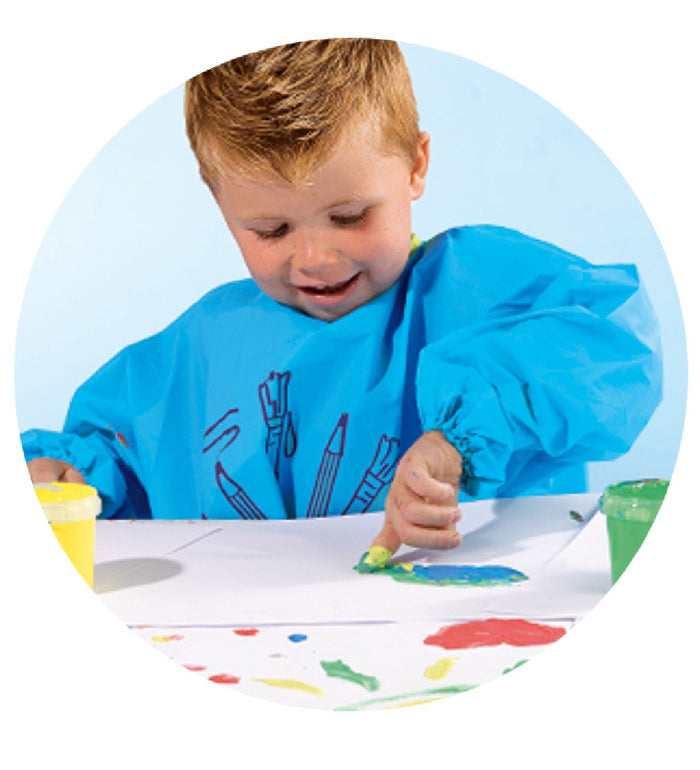 Young child in a blue smock finger painting on paper with pots of green and yellow paint nearby.