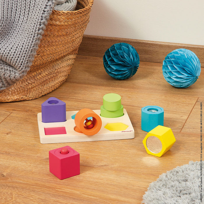 Colorful wooden puzzle tray with six sensory blocks in shapes like a pink cube, orange bell, and yellow mirror.