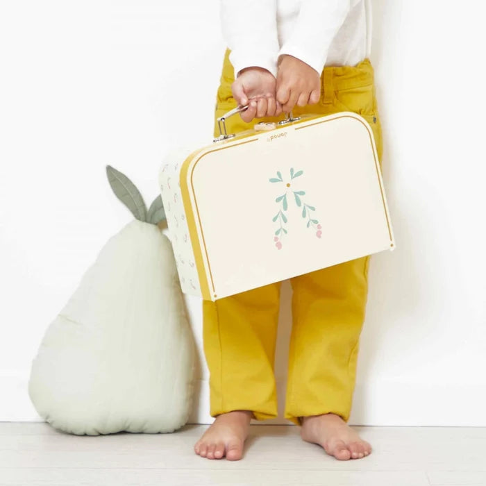 Child holding a cream toy suitcase with yellow trim and floral design next to a large pear-shaped plush toy.