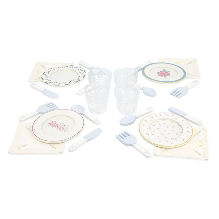 Pastel toy dinnerware set for four with floral plates, wooden cutlery, fabric napkins, and clear glasses.