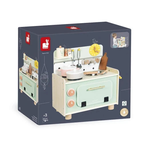 Janod toy kitchenette box featuring a light green wooden play kitchen with accessories, knobs, and a clock.