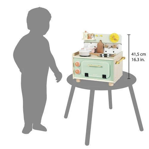 Light green and wood toy kitchen with oven and stove on a table next to a child silhouette, measuring 16.3 inches tall.