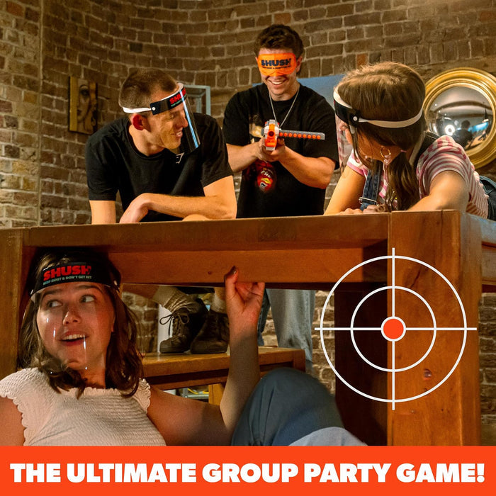 Four people play a party game with toy blasters, blindfolds, and face shields around a large wooden table.