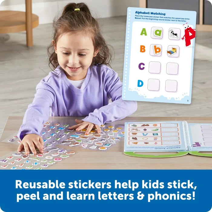 Smiling girl uses colorful reusable stickers to match letters and pictures in an alphabet activity book.
