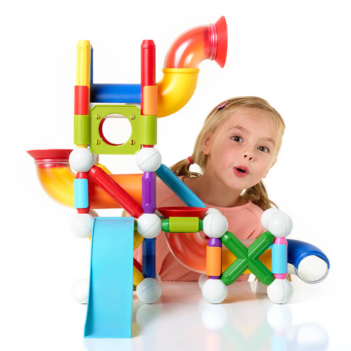 Surprised girl behind a colorful magnetic toy with bright rods, white spheres, curved tubes, and a blue slide.