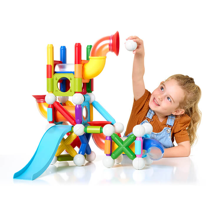 Girl drops a white ball into a colorful magnetic marble run with slides, tubes, and chunky magnetic rods.
