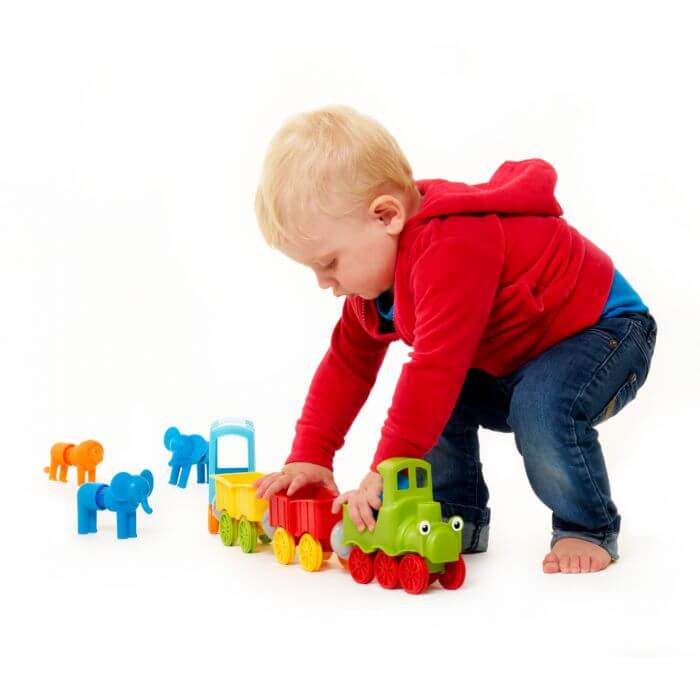 Toddler playing with a colorful magnetic toy train set with a green engine, red car, and plastic animal figures.