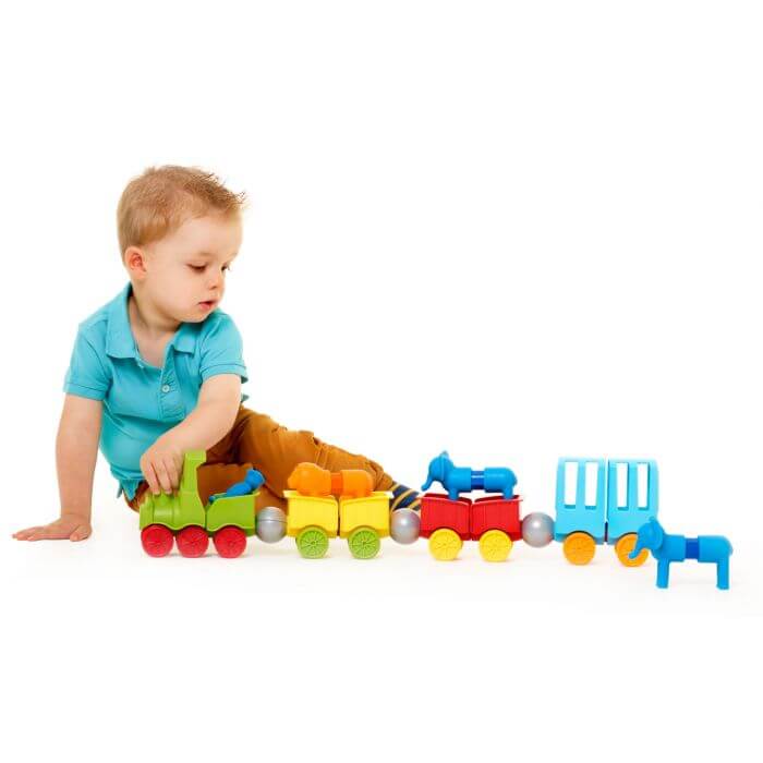 Toddler plays with a colorful magnetic toy train with a green engine, yellow and red cars, and blue animals.