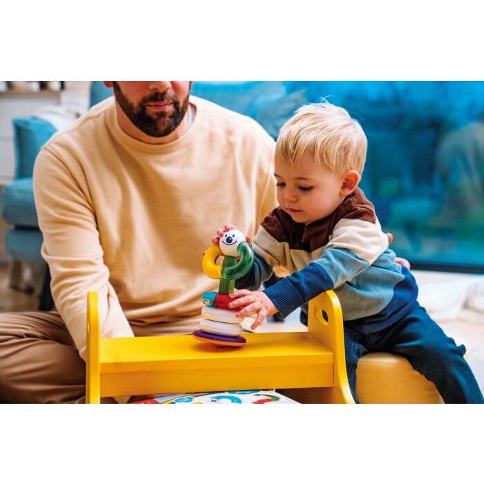 Toddler and a man play with colorful magnetic stacking rings on a small yellow table.