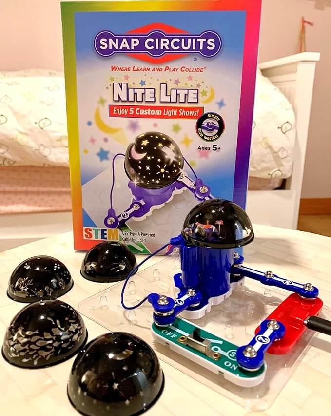 Snap Circuits box behind an assembled toy circuit and five black projection domes with moon and star cutout patterns.