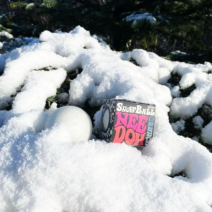 White speckled round squishy ball and its black and pink packaging box sitting in fluffy white snow.