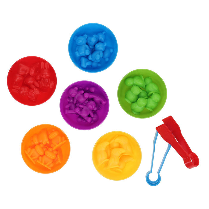 Six rainbow-colored bowls filled with matching toy animal figures and two sorting tweezers on a white background.