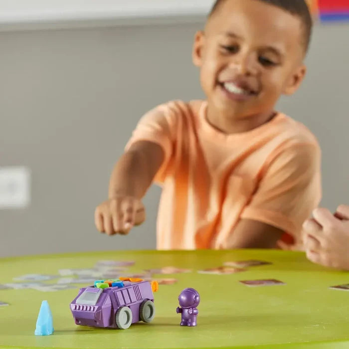 A child reaches for a purple toy rover and astronaut figure on a green table with colorful coding cards.