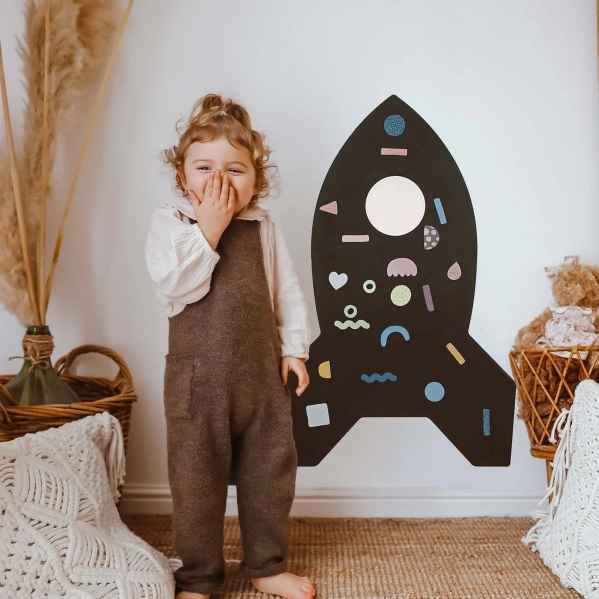 Black rocket-shaped magnetic wall board with colorful geometric magnets and a white circular window.