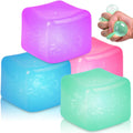 Four colorful, translucent squishy cubes in purple, pink, blue, and green, with a hand squeezing the green cube.