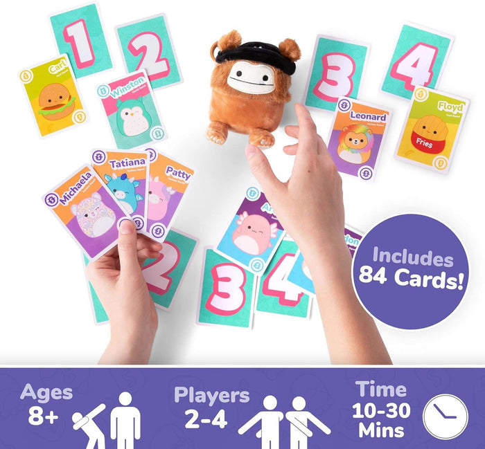 Hands playing with colorful Squishmallows character cards, numbered cards, and a small brown plush toy in the center.