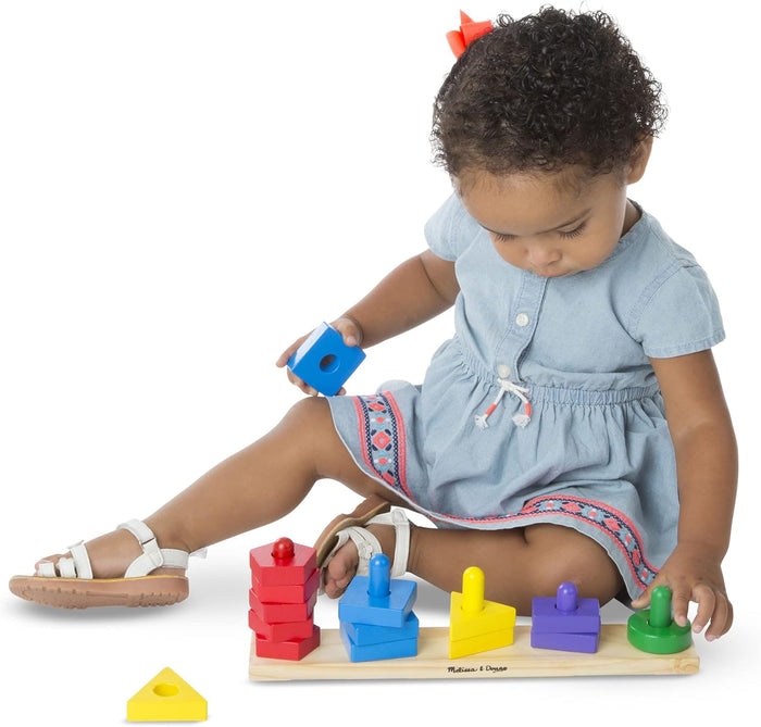 A toddler girl plays with colorful wooden geometric blocks on a wooden sorting board with pegs.