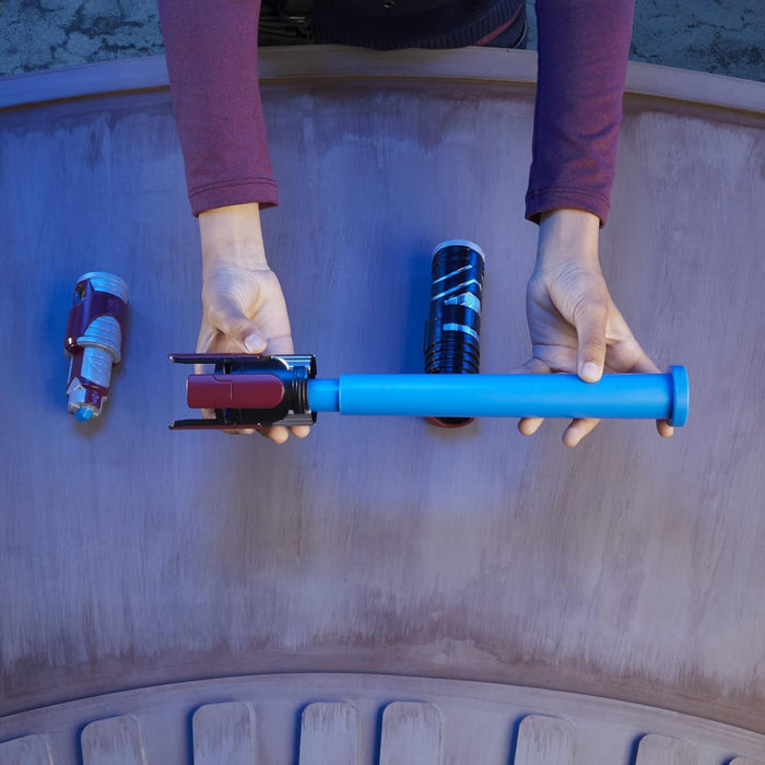 Hands assembling a modular blue toy lightsaber with maroon and black hilt components on a flat surface.