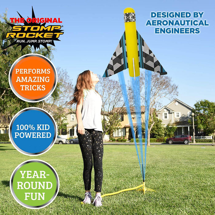 A girl watches a yellow and black checkered toy plane launch from a foot-powered pump in a sunny neighborhood park.