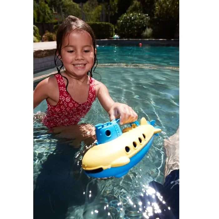 Smiling girl in a swimming pool playing with a yellow and blue toy submarine with a handle and portholes.