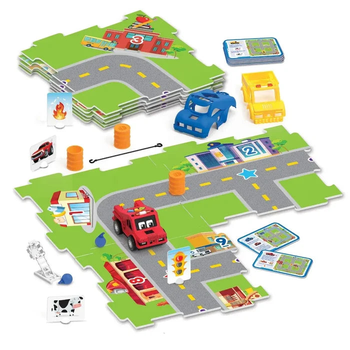 Red toy car on modular town map tiles with blue and yellow shells, challenge cards, and plastic traffic accessories.