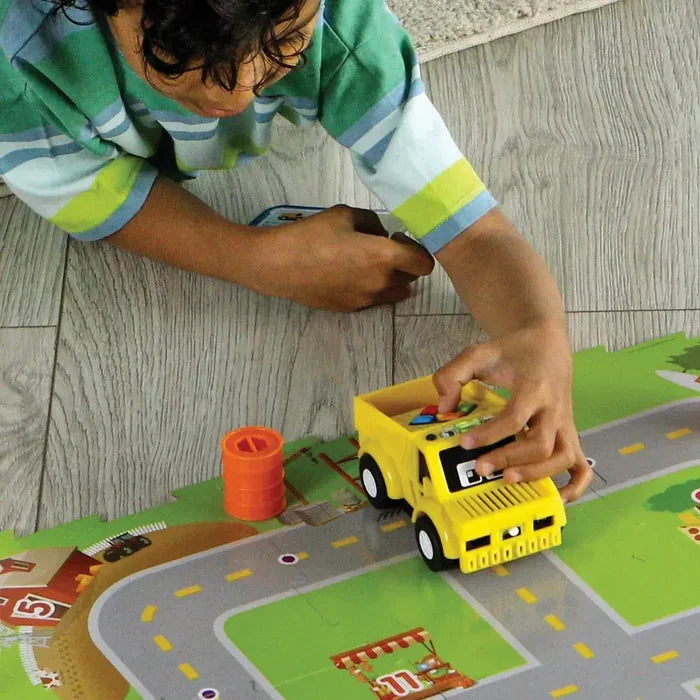 Child playing with a yellow toy truck and colorful coding tiles on a vibrant road-themed play mat.