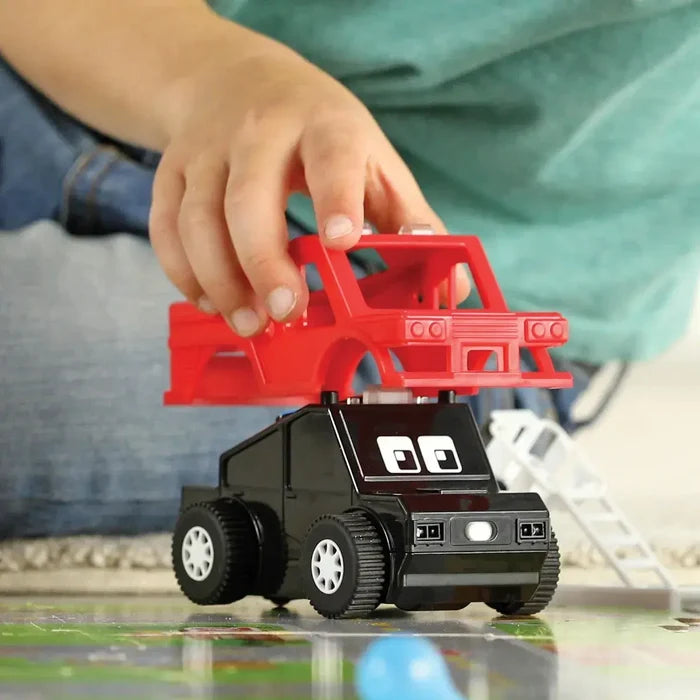 Child's hand attaching a red truck shell to a black toy car base with large wheels and cartoon eyes.