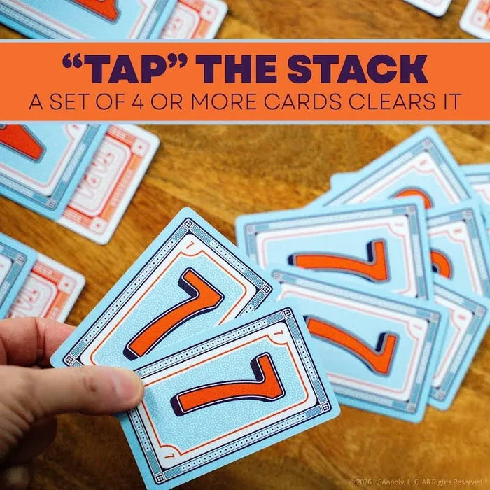 Hand holding two light blue cards with orange 7s over a scattered pile of cards on a wooden surface.