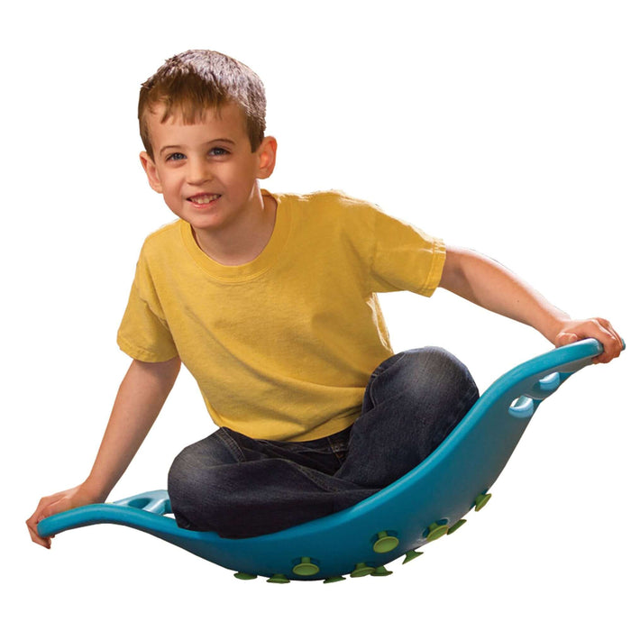A child sits on a blue curved balance board with green suction cups on the bottom and integrated handles.