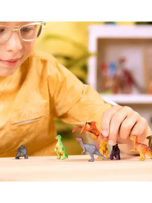 Child playing with miniature colorful plastic dinosaur toys, holding an orange pterodactyl over a grey dinosaur.
