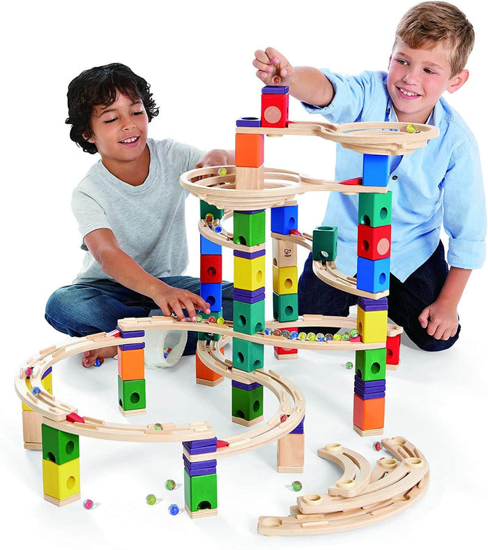 Two boys playing with a tall wooden marble run featuring colorful blocks, spiral tracks, and glass marbles.