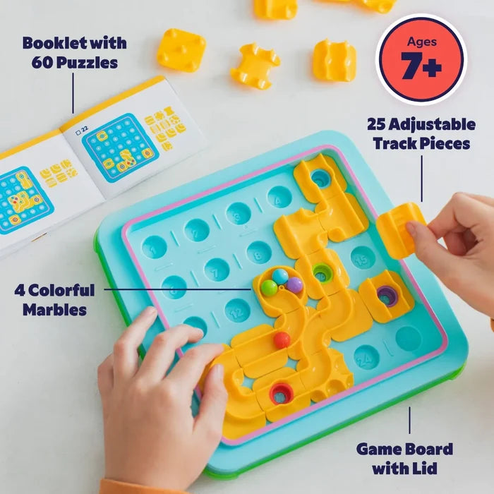 Hands arrange yellow track pieces on a blue game board with four colorful marbles and a puzzle instruction booklet.