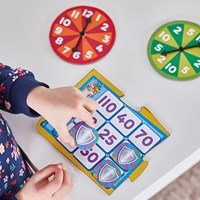 Child placing shield tokens on a numbered grid board next to red and green circular spinning wheels.