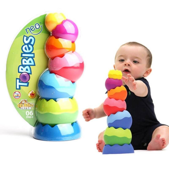 Colorful, textured nesting spheres in packaging beside a baby stacking the vibrant pieces into a wobbly tower.