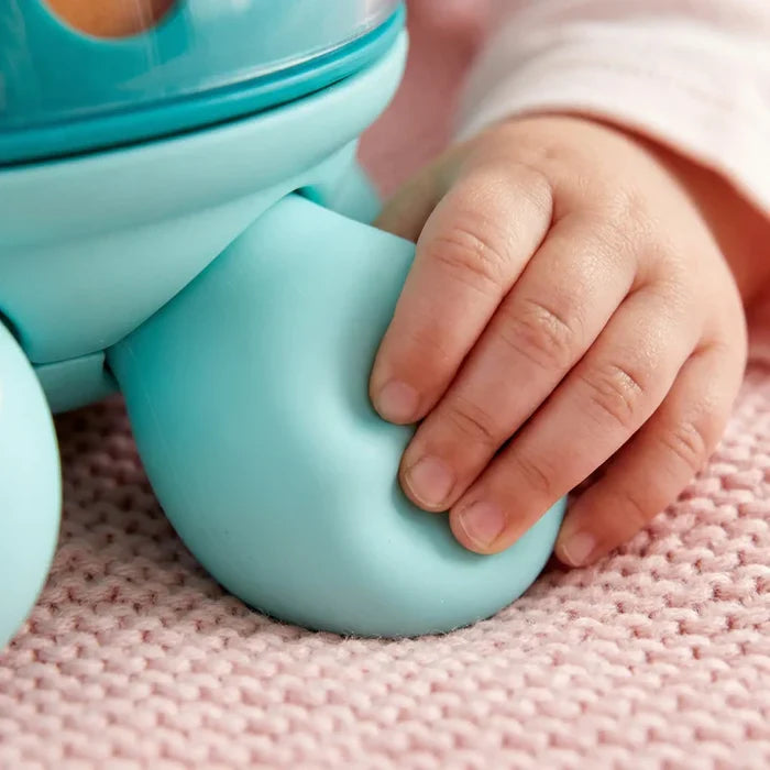 Baby hand touching the smooth, light blue leg of a turtle toy on a pink knitted blanket.