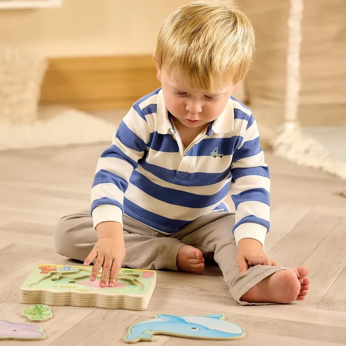 Toddler plays with chunky wooden puzzle pieces of a blue whale and green sea turtle on a light wood floor.