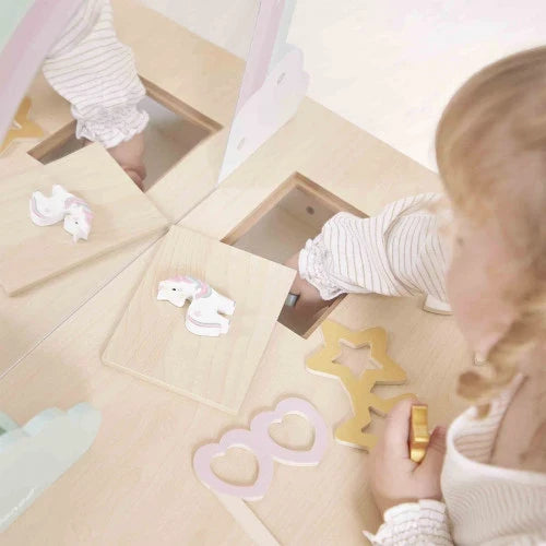 Child playing with a light wood vanity toy featuring pastel unicorn, heart, and star-shaped wooden accessories.