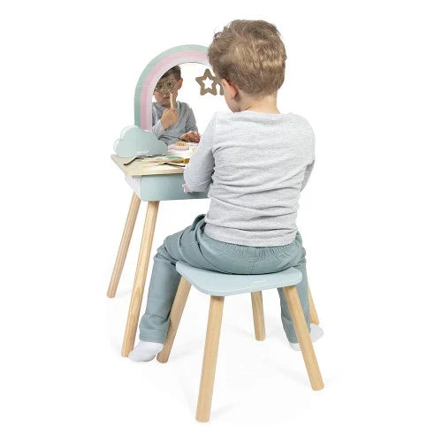 Child sitting on a small wooden stool at a light blue rainbow vanity table with matching toy accessories.